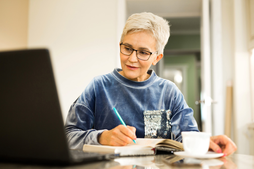 Stylish older woman with a short haircut sits at a table with a laptop