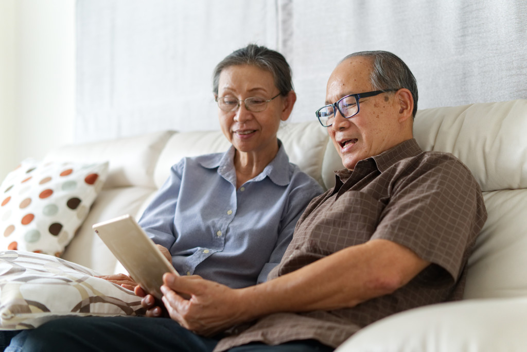 Senior couple sitting on sofa in home using a tablet