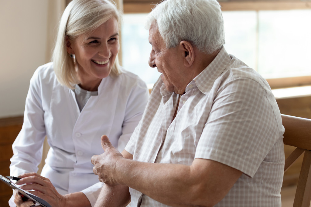Elderly man patient and middle-aged nurse talking indoors