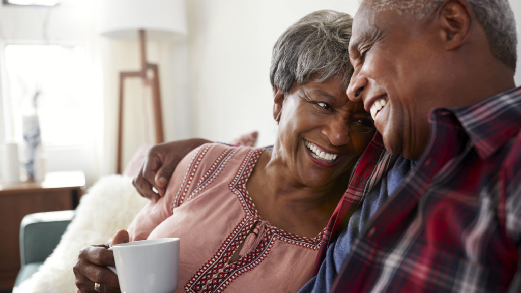 senior couple laughing and drinking coffee together on couch