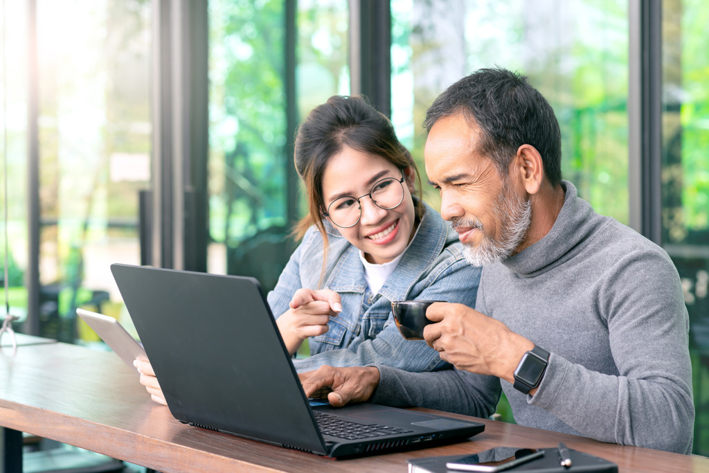 mature man with white stylish short beard looking at laptop computer with woman in cafe