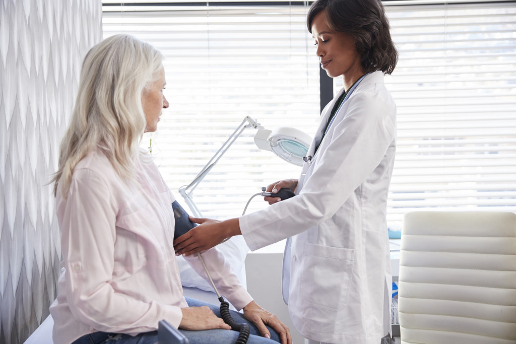 Woman Patient Having Blood Pressure Taken By Female Doctor In Office