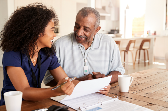 Smiling female caregiver in scrubs looks over older adult woman's shoulder at tablet