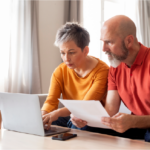 Mature couple reviewing paperwork together at desk with laptop