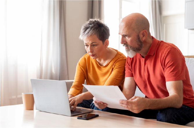 Mature couple reviewing paperwork together at desk with laptop