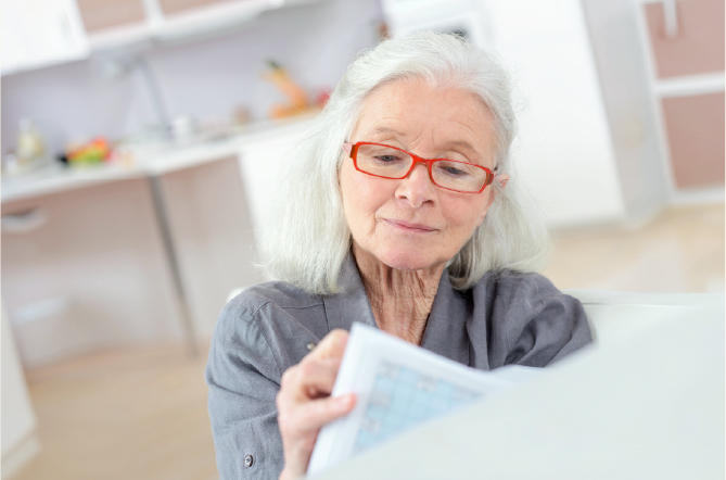 Older adult woman wearing red glasses writing in planner at home
